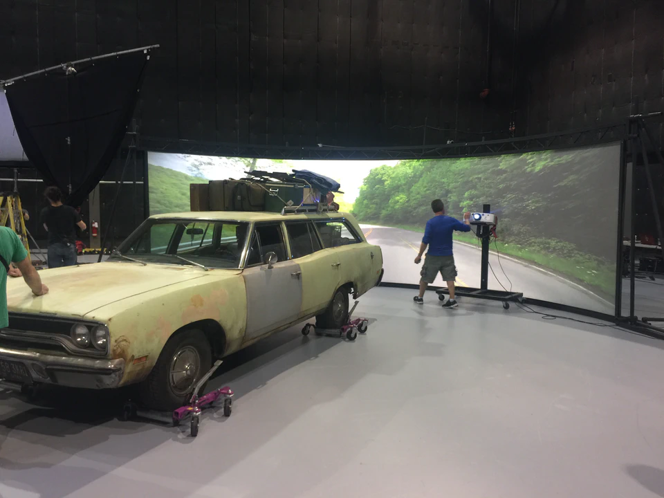 A station wagon on The Glass Castle studio set in front of a curved rear-projection screen displaying a road scene.
